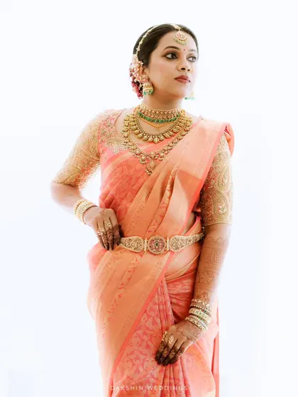 A regal portrait of a bride in a peach Kanjeevaram saree, showcasing her elaborate jewelry and confident posture.