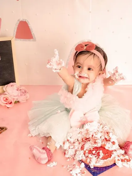 A princess deserves a royal mess! This little girl is joyfully smashing her first birthday cake in our pink castle-themed studio setup, complete with a beautiful dress and all.