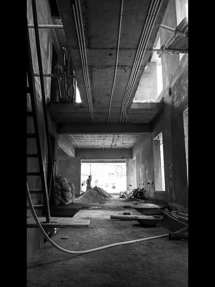 An atmospheric black and white shot of an interior under construction, showing the exposed ceiling beams, conduits, and the play of light in the unfinished space.
