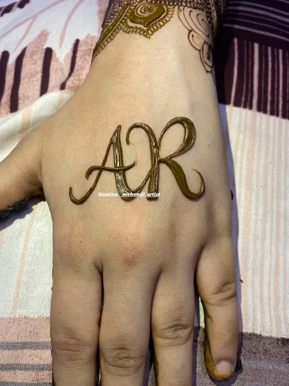 The initials 'AR' are the star of this design, drawn in a flowing script on the back of the hand.