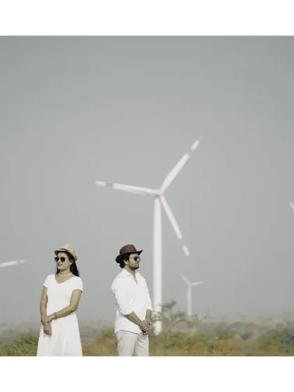 A minimalist and artistic pre-wedding shot, with the couple standing apart but connected in a field of windmills.