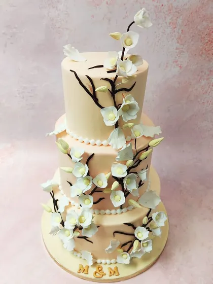 We create a breathtaking centerpiece with this three-tiered cherry blossom wedding cake. Delicate, handcrafted sugar cherry blossoms gracefully climb dark branches against a soft blush-colored fondant, embodying the beauty and elegance of a spring wedding.