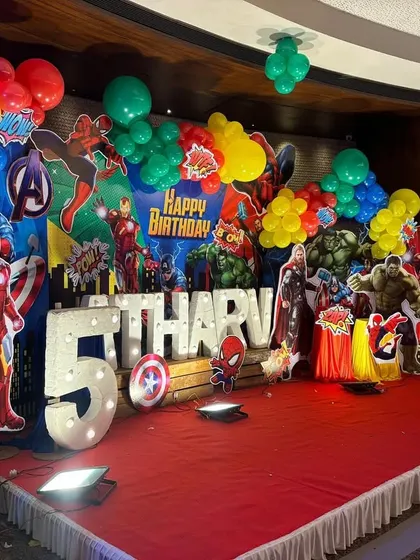 A side angle of the superhero stage, showing the layered arrangement of character cutouts and balloon clusters that create a 3D effect.
