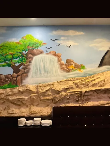 A section of the Drool Kitchen mural, showing the hand-painted waterfall and surrounding nature. The textured wall underneath adds to the rugged, natural feel of the landscape.
