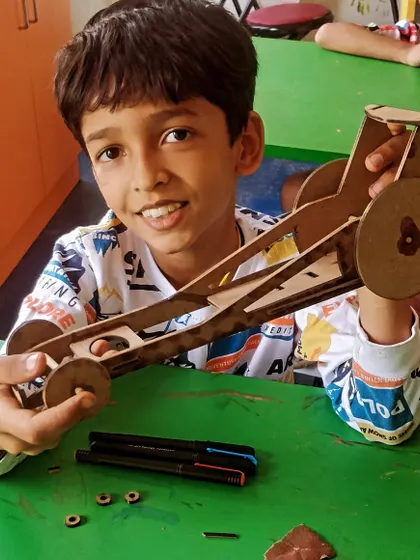 This student smiles with his completed wooden car project, ready to add some finishing touches.
