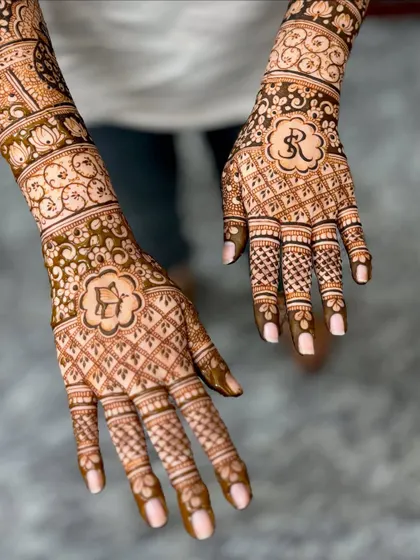 Renuka's wedding mehendi, personalized with the couple's initials "R" and a butterfly, set within a floral frame.