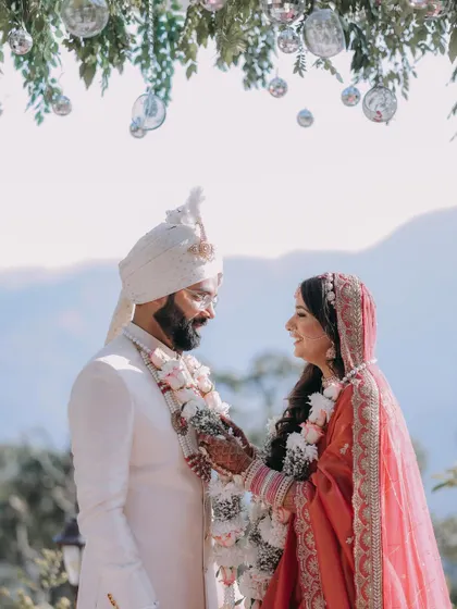 The couple shares a smile during their jaimala exchange at their outdoor mountain wedding.