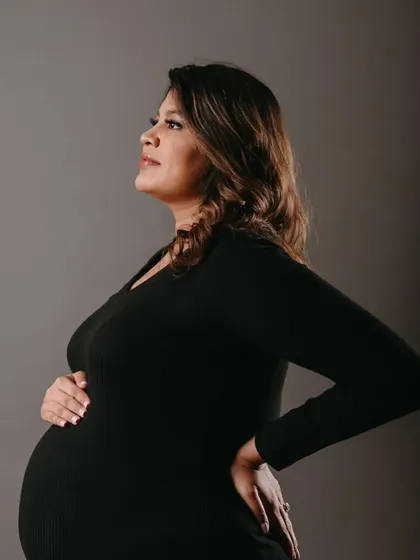 A side profile showcasing her beautiful baby bump. The makeup is elegant and understated, creating a look of pure grace.