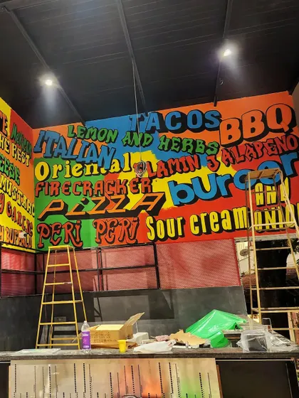 A shot of the right side of the menu wall, featuring words like "Tacos," "Pizza," and "Peri Peri" in bright, eye-catching colors.