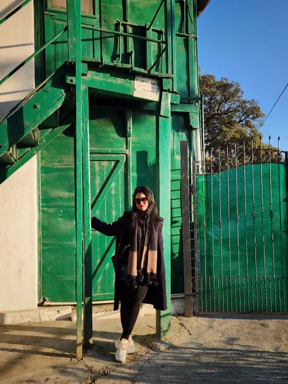 An all-black winter outfit against a vibrant green building in Mussoorie creates a striking visual contrast.