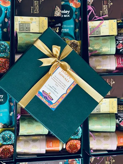 This top-down shot shows the striking contrast of the gold ribbon against the deep green box, surrounded by the contents of other hampers.
