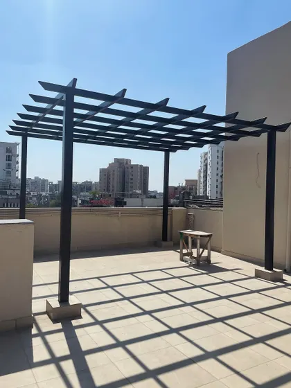 The foundational structure of a rafter pergola on a city terrace. This simple yet strong metal frame is the first step in creating a shaded and defined outdoor living area.