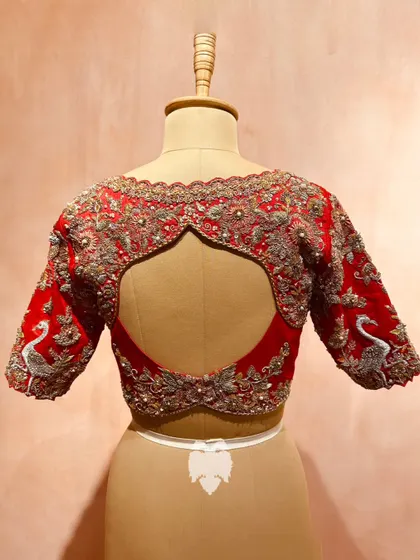 The back of a scarlet red blouse, where the scalloped neckline is adorned with floral embroidery and the sleeves feature majestic swans.