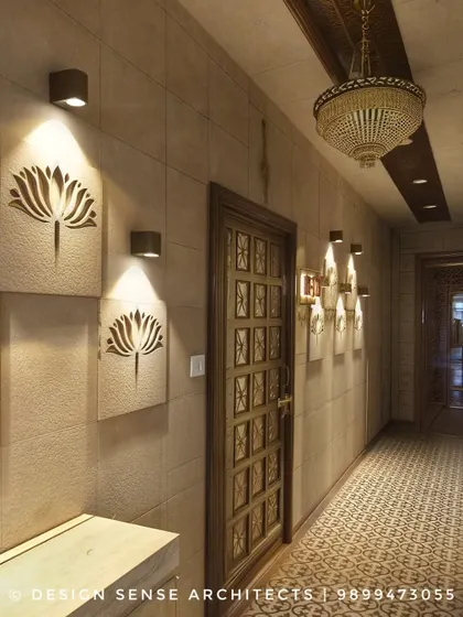 An elegant hallway featuring custom sandstone panels with a lotus motif, spotlit for dramatic effect. The traditional floor tiles and ornate door complete this Indian-inspired design.
