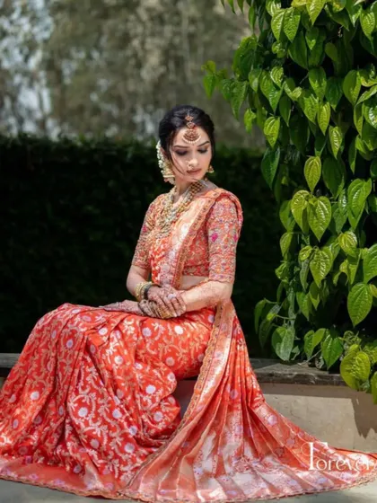 A beautiful shot of the bride in her vibrant orange saree. The makeup is kept warm and glowing to match the richness of her outfit.