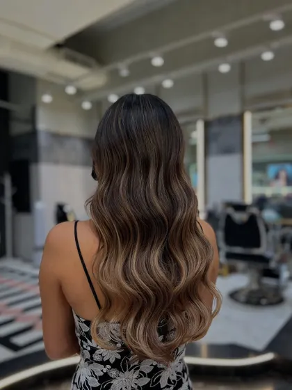 A stunning Redken balayage transformation. The 'after' shot shows a beautiful gradient from dark roots to lighter, ash-toned ends, styled in perfect waves.