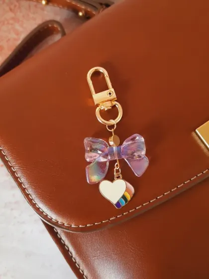 Another look at the iridescent bow and rainbow heart charm, showing how it catches the light on a leather bag.