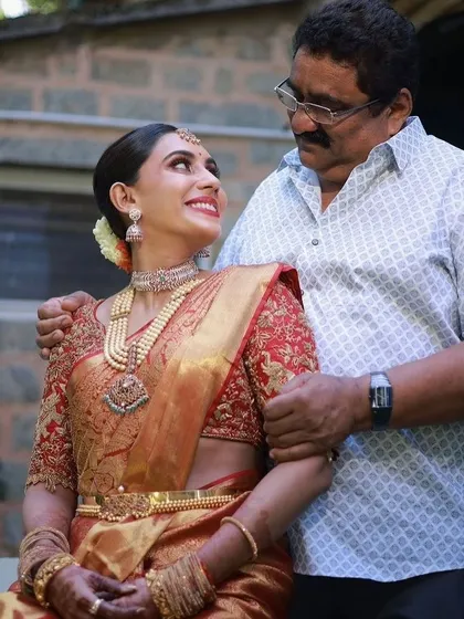 A precious moment between a bride and her father. Her custom red embroidered blouse and Kanchivaram saree create a look of timeless elegance for her wedding day.