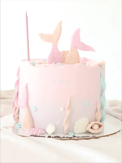 A minimal and aesthetic mermaid cake. The soft pink ombre is decorated with beautifully crafted fondant mermaid tails, seashells, and starfish in pastel shades.