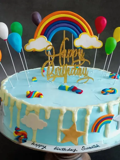 A fun rainbow-themed cake with balloon toppers and a white chocolate drip.