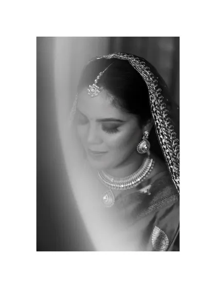 A soft, ethereal black and white bridal portrait. The light flare and gentle focus give this image a dreamy and timeless quality, highlighting the bride's serene beauty.
