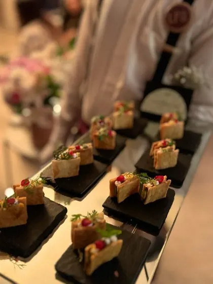 A tray of mini tacos filled with a savory mixture and topped with pomegranate seeds and microgreens. These bite-sized tacos are a fun and flavorful addition to any event, from a casual get-together to a festive celebration.