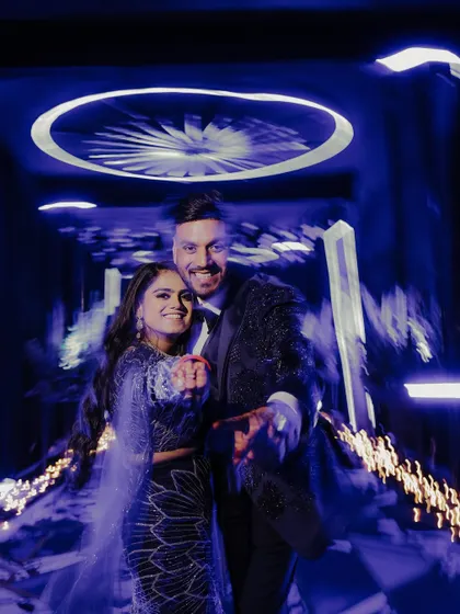 A fun and energetic candid shot of the couple. They point towards the camera with big smiles, captured with a creative motion blur effect that conveys the fast-paced excitement of the party.