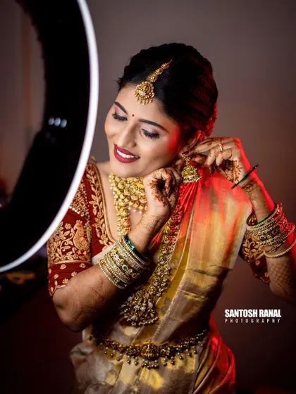 A joyful getting-ready shot of the bride putting on her earrings, with a ring light creating a beautiful glow.
