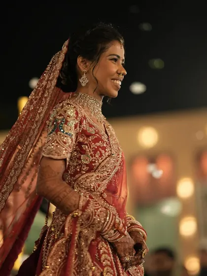 A candid shot of the bride's radiant smile during her wedding. Her intricate red lehenga and glowing makeup create a picture of pure happiness and bridal beauty.