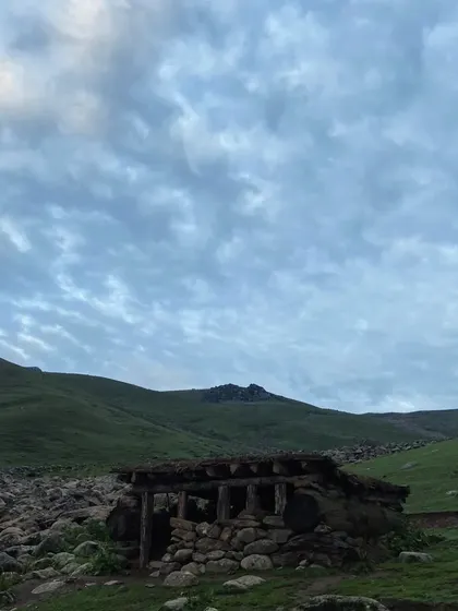A rustic stone shelter sits in the vast green meadows of Kashmir, a testament to the simple, traditional life that exists along the Great Lakes trek.