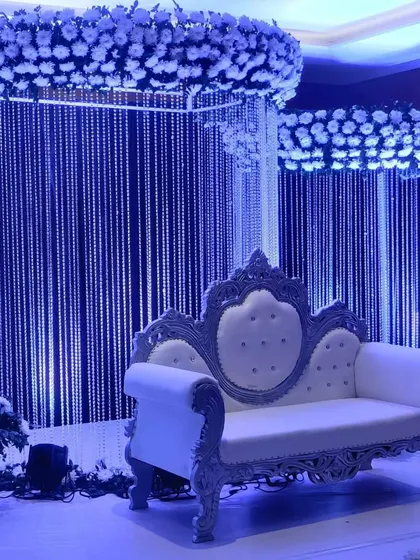 A striking reception stage design with a cool blue lighting theme. The backdrop features curtains of crystal beads, and the stage is crowned with rings of white flowers, creating a glamorous, icy effect.