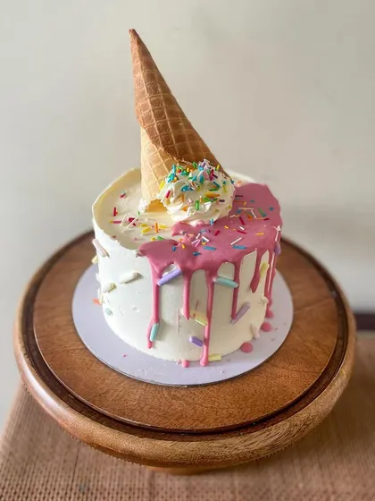 An ice cream drip cake that screams fun. This cake has a pink ganache drip, colorful sprinkles, and is topped with an upside-down ice cream cone for a playful birthday theme.
