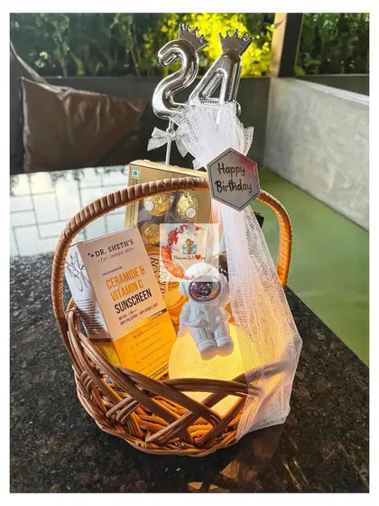 A 24th birthday basket for him, complete with a number balloon, sunscreen, an astronaut-themed night light, and Ferrero Rocher chocolates.