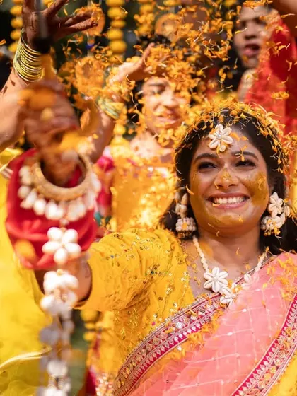 A bride's ecstatic expression as she is showered with marigold petals during her Haldi. This frame is a burst of color and pure happiness, a perfect memory of the celebration.