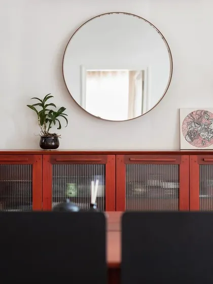 A mahogany wood credenza with fluted glass doors in our 'Rustic Minimal' project. This piece provides stylish storage while the round mirror above it enhances the sense of space and light in the dining area.