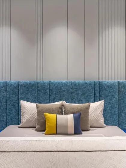 In the master bedroom, a soothing blue palette sets the tone for relaxation. The upholstered headboard is complemented by a subtle grey-paneled wall and integrated lights for a cozy atmosphere.
