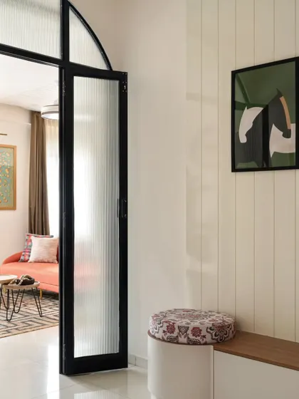 As you enter the 'Colorpop Home,' you're greeted by this sleek and minimalist foyer. A fluted glass partition with an archway leads into the living room, while a duco-paneled wall conceals a seating zone and shoe storage, blending aesthetics with practicality.