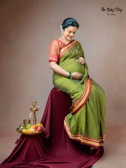 A quiet, reflective pose of the mother-to-be looking down at her bump. This shot captures the personal connection and anticipation, with the traditional props adding cultural context.