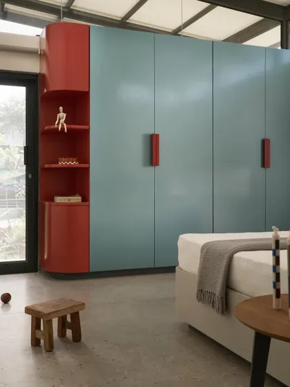 A bedroom in Pavilion House featuring bold, colorful cabinetry against a backdrop of clean lines and concrete floors. This space demonstrates how we introduce playful, personal elements within a modern architectural framework.