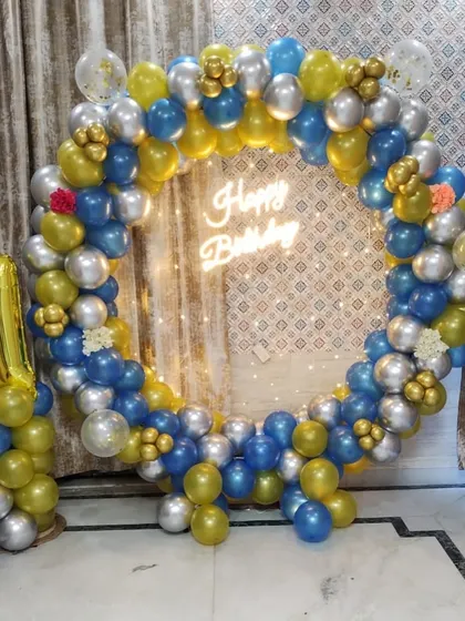 A first birthday decoration with a balloon ring in blue, gold, and silver, and a foil number "1" balloon pillar.