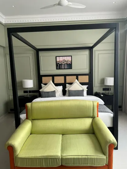 A modern hotel suite featuring a black four-poster canopy bed with a cane and wood headboard. The room is completed with a vibrant green loveseat, demonstrating my ability to work with bold colors and contemporary designs.
