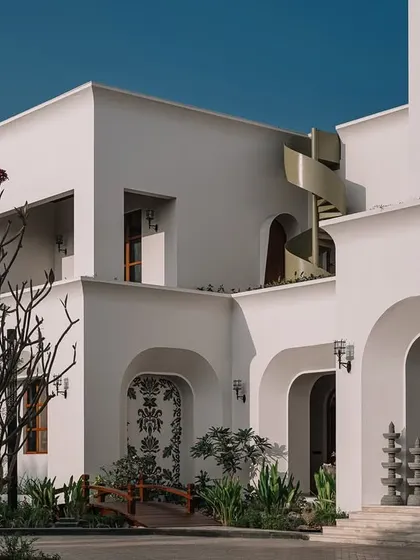 The exterior of the Rehethaan residence, showing the clean, white Mediterranean-inspired architecture, with its multiple terraces and a sculptural spiral staircase.