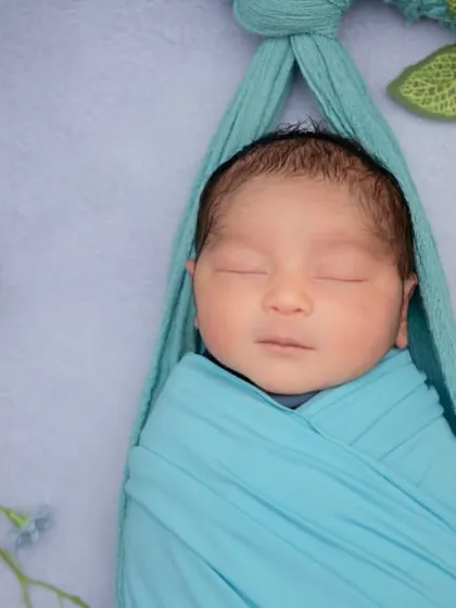 A close-up of a baby boy swaddled in blue, hanging peacefully in a sling. His serene face is the picture of calm and tranquility.