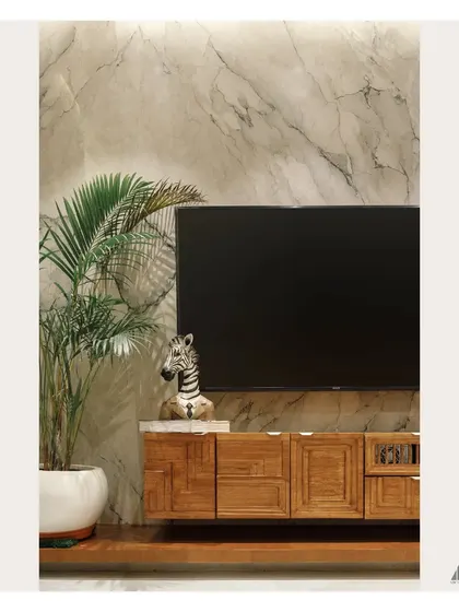 A detail shot of the living room's TV wall. The authentic, veined marble provides a poetic backdrop for the custom-carved wooden media unit, accented by a potted palm to bring a touch of nature indoors.