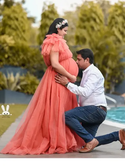 A tender moment between a couple, with the mom-to-be in a lovely coral-pink tulle gown. The one-shoulder design and soft fabric create a gentle and romantic look.