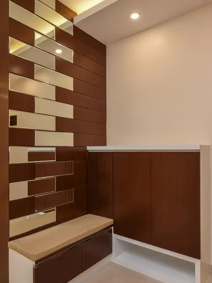 A functional foyer design with a built-in shoe rack that includes a comfortable seating bench. The partition wall with wood and mirror panels adds a decorative touch while separating the entryway from the main living area.