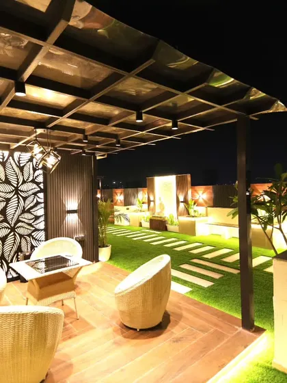 A night view of the completed pergola and lounge area in our Sushant Lok project, featuring wicker chairs and decorative wall panels.