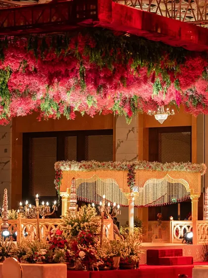 A traditional mandap structure is elevated by a lush ceiling of red and green florals. This design focuses on creating a sacred space that is both grand and intimate, perfect for a heritage wedding.