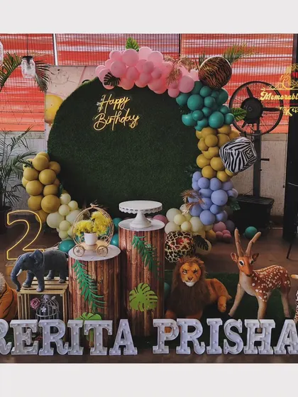 A wide shot of the trendy forest-themed birthday party, showing the full arrangement of animal props, a moss backdrop, and colorful balloons.