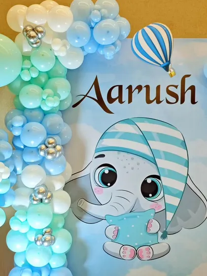 A close-up of the sleepy baby elephant character from Aarush's party, set against a backdrop of blue and mint green balloons.